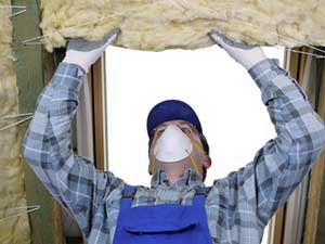 Contractor installing insulation in an attic while wearing a white face mask.